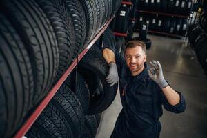 In professional, uniform near the shelve. Man worker is maintenance station with tires, wheels photo