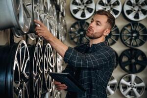 Manager is checking, the product, with digital tablet. Man worker is maintenance station with tires, wheels photo