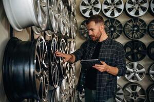 Manager, is checking the product, with digital tablet. Man worker is maintenance station with tires, wheels photo