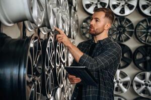 Manager is, checking the product, with digital tablet. Man worker is maintenance station with tires, wheels photo
