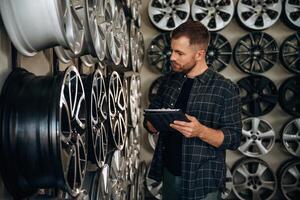 Manager, is ,checking the product, with digital tablet. Man worker is maintenance station with tires, wheels photo