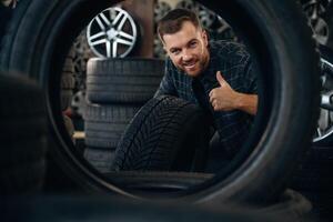 Smiling,,, positive facial expression, hand gesture. Man worker is maintenance station with tires, wheels photo