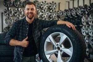 Smiling,, positive facial expression, hand gesture. Man worker is maintenance station with tires, wheels photo