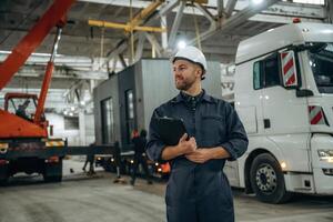 Front view, holding ,,,notepad, standing. Male worker is in the modern warehouse or manufacturing company photo
