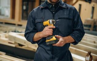 Small drill in hands. Male ,,,builder is at construction of wooden house photo
