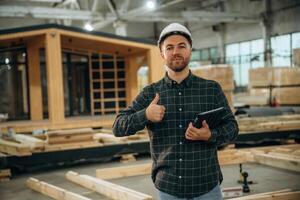 Digital, tablet is ,in hand. Male builder is at construction of wooden house photo