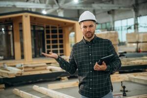 Digital, tablet is in hand. Male,, builder is at construction of wooden house photo
