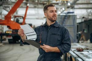 Front, view, holding ,notepad, standing. Male worker is in the modern warehouse or manufacturing company photo