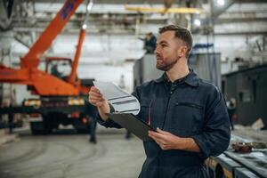 Front view,,, holding notepad, standing. Male worker is in the modern warehouse or manufacturing company photo