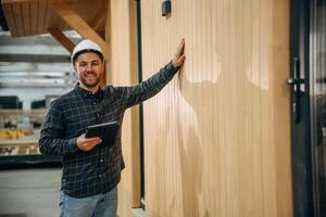 Digital tablet, is in hand. Male builder is at construction of wooden house photo