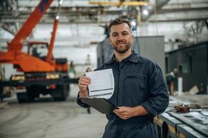 Fron,,t view, holding notepad, standing. Male worker is in the modern warehouse or manufacturing company photo