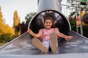 A happy child girl playing on a slide on the park playground. photo