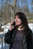Young woman talking on phone in a sunny park surrounded by trees during spring photo