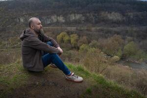Man sits quietly by a riverbank overlooking a serene landscape in early spring photo