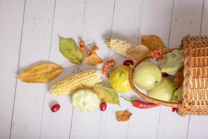 Top view autumn harvest basket with corn, apples, zucchini and peppers on a wooden background decorated autumn leaves photo