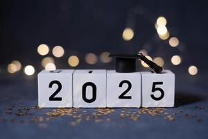Class of 2025 concept. Wooden cubes 2025 with graduate hat on dark background with bokeh photo