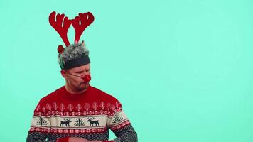 Man wears red New Year sweater deer showing thumbs up and pointing at on blank advertisement space video