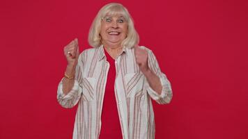 Stylish senior old woman shouting, raising fists in gesture I did it, celebrating success winning video