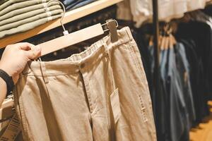 hand holding a pair of beige chino pants on a hanger in a clothing store. The image captures the relaxed texture of the fabric and the casual style of the garment, ideal for everyday wear. photo
