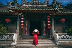 A woman in a traditional Vietnamese costume and a conical hat on the background of an ancient building in Hoi An, Vietnam. photo