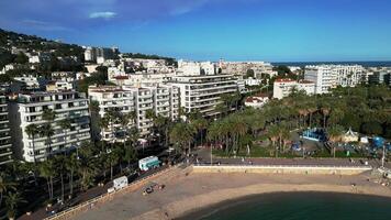 Aerial view of the azure coastline and cityscape of Cannes, France. The scene includes sandy beaches, palm trees, and modern buildings along the shore. Website backgrounds, YouTube vlogs, relaxation video