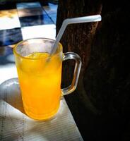 A glass of orange juice with a straw in it. The glass is half full and the straw is in the middle of the glass photo