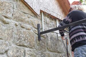 man installs iron brackets for the outdoor unit of an air conditioner on the wall of a stone house. Home microclimate and cooling in summer photo