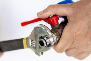 Hand with wrench adjusting metal faucet with red handle on pipe. Plumbing repair photo