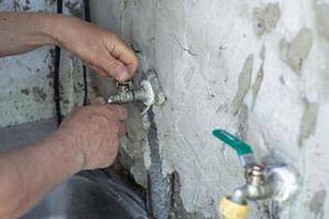 man repairs a faucet by tightening it on an old wall with a wrench photo