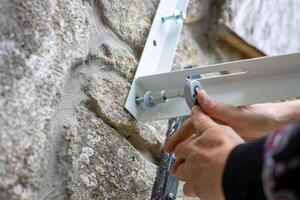 man uses a ratchet wrench with a socket to screw a screw into a metal bracket to install an air conditioner on the stone wall of a rural home. photo