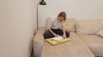 Creative professional relaxing on comfortable sofa, sketching design ideas in notebook while occasionally responding to phone communication during peaceful working from home moment video