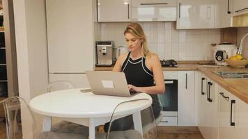 Professional businesswoman working remotely, typing on laptop while sitting at kitchen table, embodying modern digital nomad lifestyle and home office productivity video