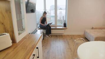Productive home office environment with young professional woman working intently on laptop, benefiting from bright natural window light while maintaining comfortable, focused workspace video