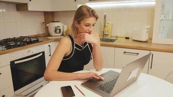 Professional businesswoman working intently on laptop while sitting at modern kitchen table, embodying contemporary remote work lifestyle and digital connectivity video