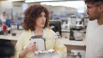 Young couple browsing kitchen appliances, holding hand mixer while discussing electronics store selection, sharing moments of collaborative shopping and decision-making in slow motion video