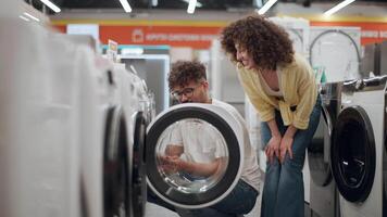 Couple browsing modern washing machines together, standing close and carefully examining features while sharing enthusiasm for new home appliance in bright retail electronics store video