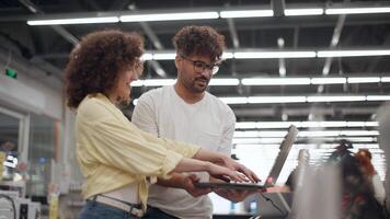 Attentive young couple comparing laptop features, moving through sleek electronics store with careful consideration of digital device options and potential purchase video