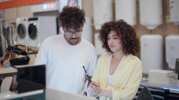 Young couple choosing electric toothbrush in electronics store, woman holding toothbrush and reading instructions on box, man watching her, slow motion video