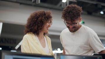 Cheerful young partners browsing laptop selection, carefully examining screen, sharing excited moments while shopping for new technology in modern electronics store video