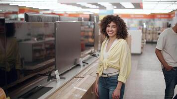 Female customer smiling brightly while browsing television display in electronics store, capturing moment of joyful retail technology shopping experience with slow motion perspective video