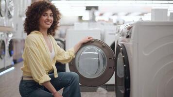Woman browsing washing machine models in electronics store, carefully touching and inspecting different options, evaluating potential purchase with focused attention in slow motion video