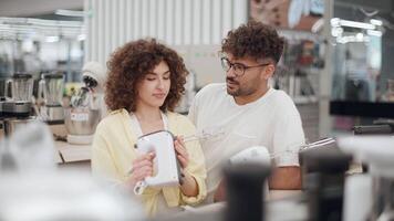 Cheerful couple standing together, browsing hand mixer selection in bright electronics store, discussing potential purchase with shared excitement video