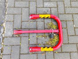 A red and yellow parking meter with a lock on it. The lock is missing. The meter is on a brick sidewalk photo