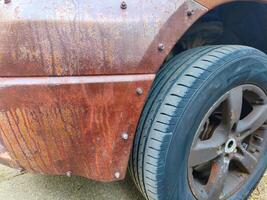A car with a black tire and a black rim has a rusty exterior. The car appears to be old and has been exposed to the elements for a long time photo