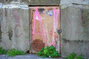 A rusty door with graffiti on it. The door is open and has a padlock on it photo