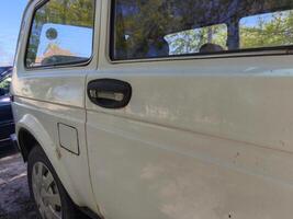 A white car with a black handle on the door. The car is parked in front of a building photo