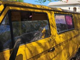 A yellow van with a red window. The van is parked in front of a house. The van is dirty and has a worn-out appearance photo