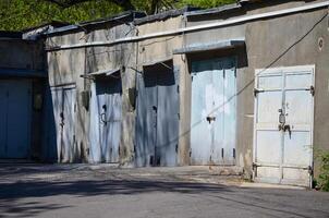 A row of blue doors are open to the street. The doors are old and rusted. The building is empty and abandoned photo