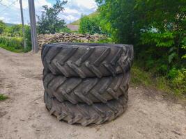 Three large black tires are stacked on top of each other. The tires are old and worn, and they are sitting on a dirt road. The scene is quiet and peaceful, with no one around photo