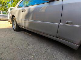 A silver car with a white stripe on the side. The car is parked in front of a white car photo